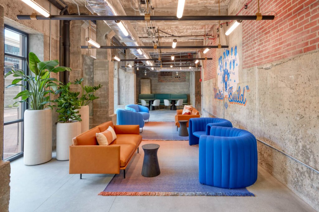 A room with concrete walls and curved blue armchairs and a leather couch