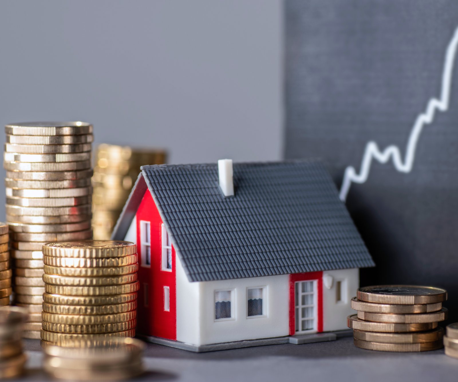 model of white, grey and red house with coins piled up next to it