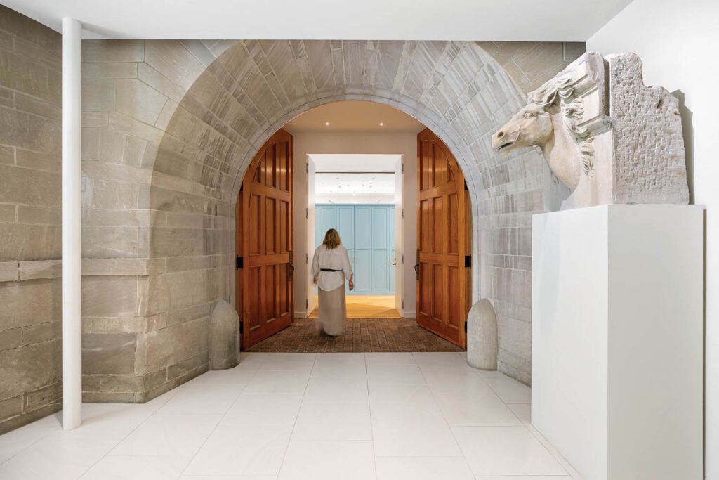 A woman walking through an arched stone entrance to an old carraiage house in a museum in an old mansion