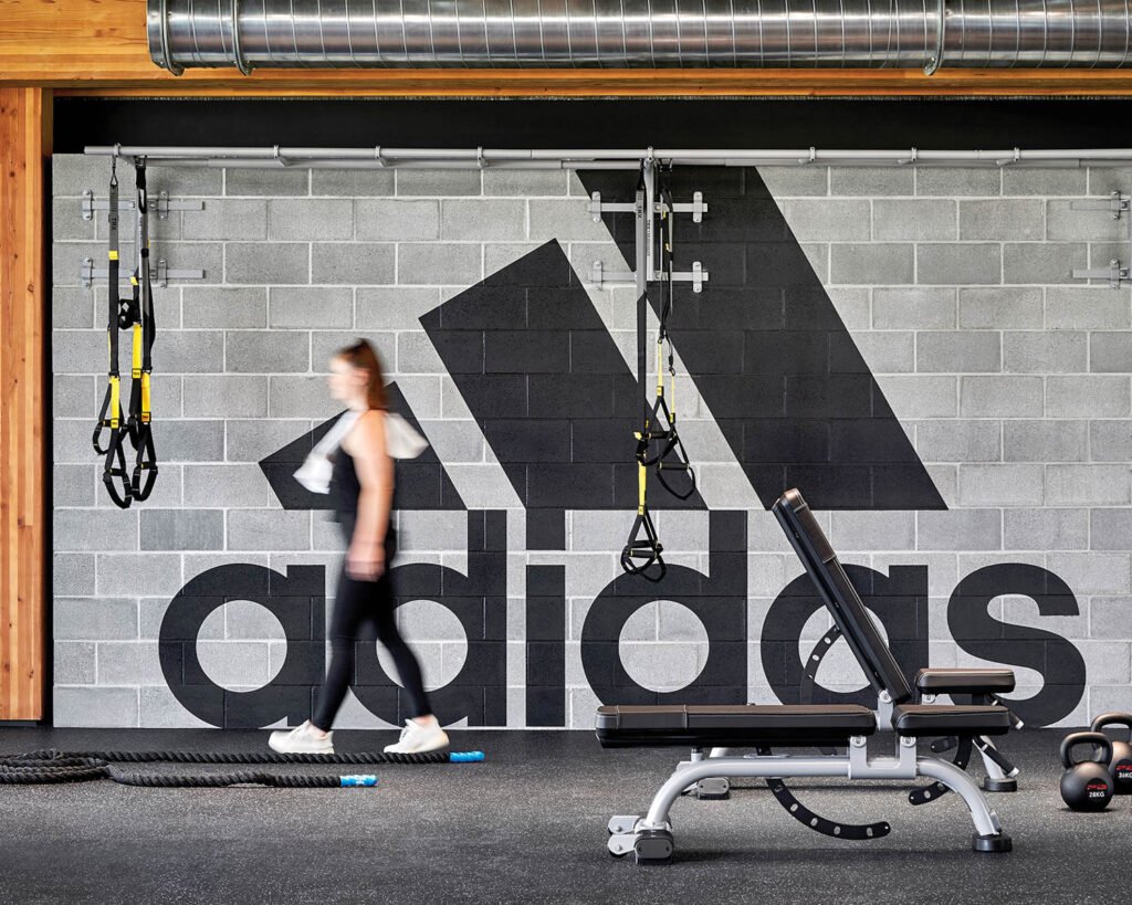 a woman in gym clothes near a wall with the adidas logo