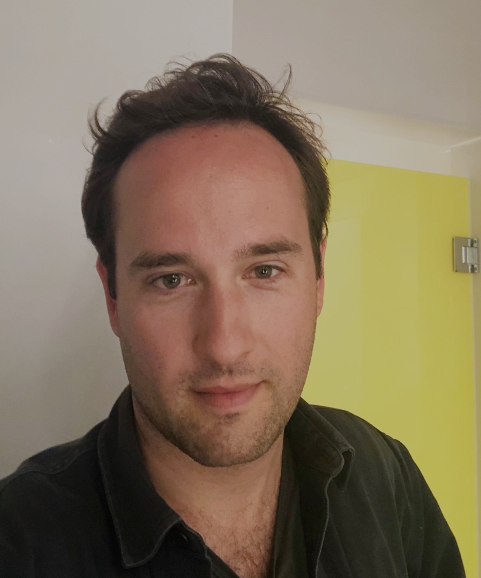 headshot of man wearing black polo shirt