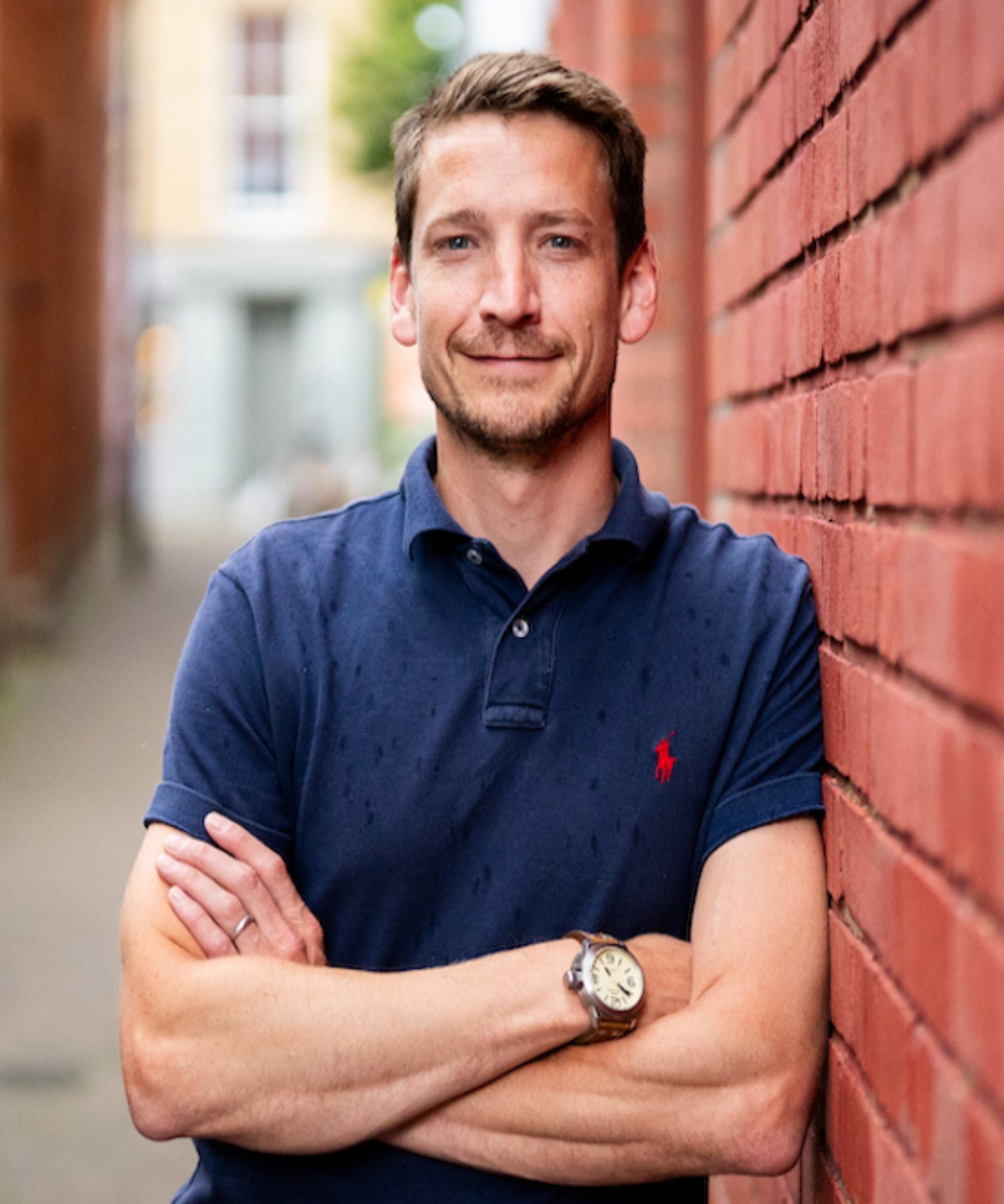 headshot of male leaning against brick wall wearing blue polo shirt