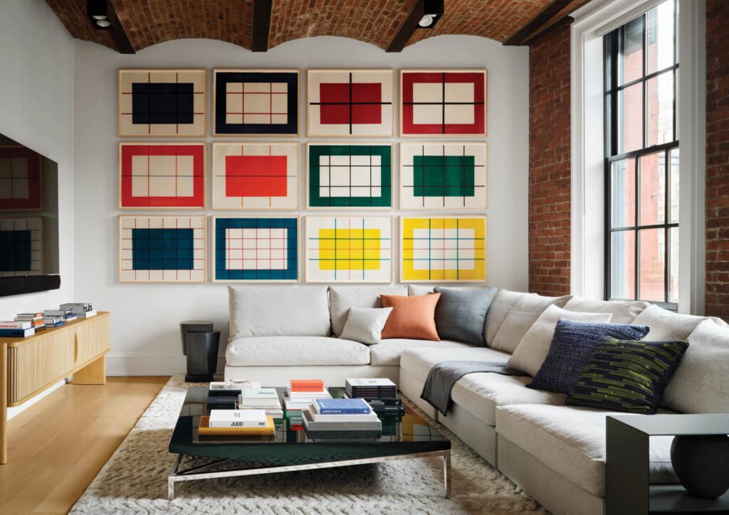 family room with a long white sectional and multiple colorful woodcuts on the wall