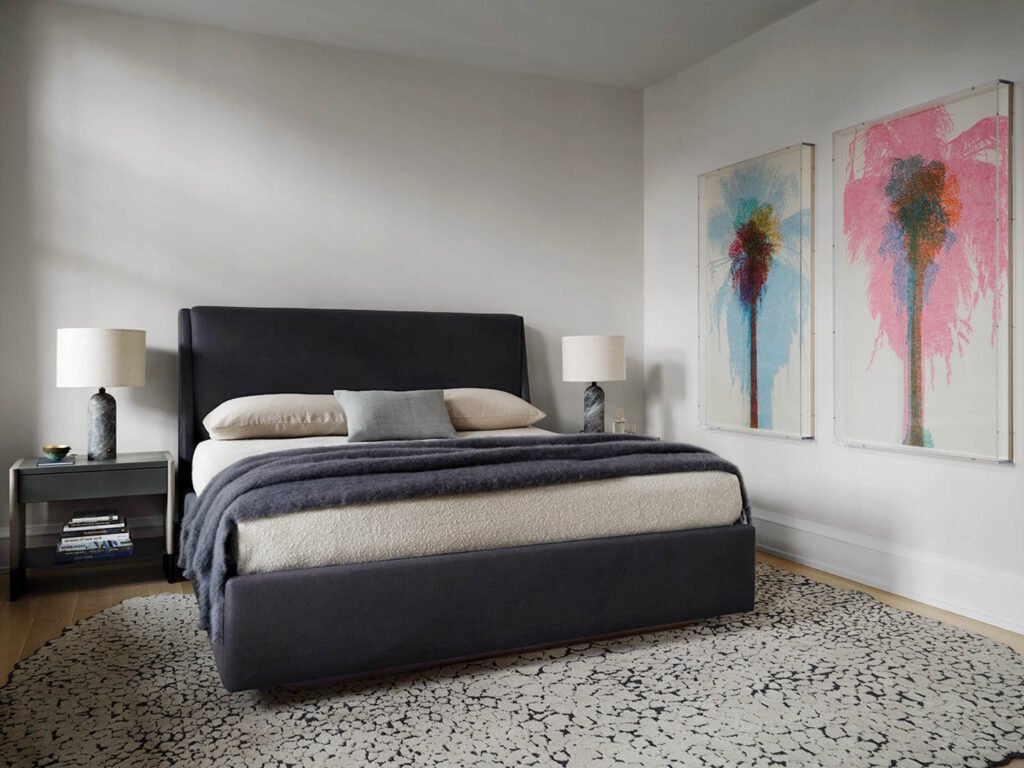 guest bedroom with dark blue sheets and colorful watercolor paintings on wall