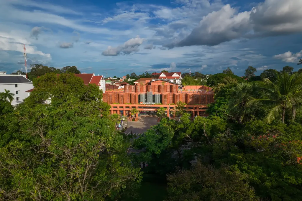 Wide exterior view of Angkor Market surrounded by greenery, highlighting the terracotta brise-soleil and rhythmic design of the structure